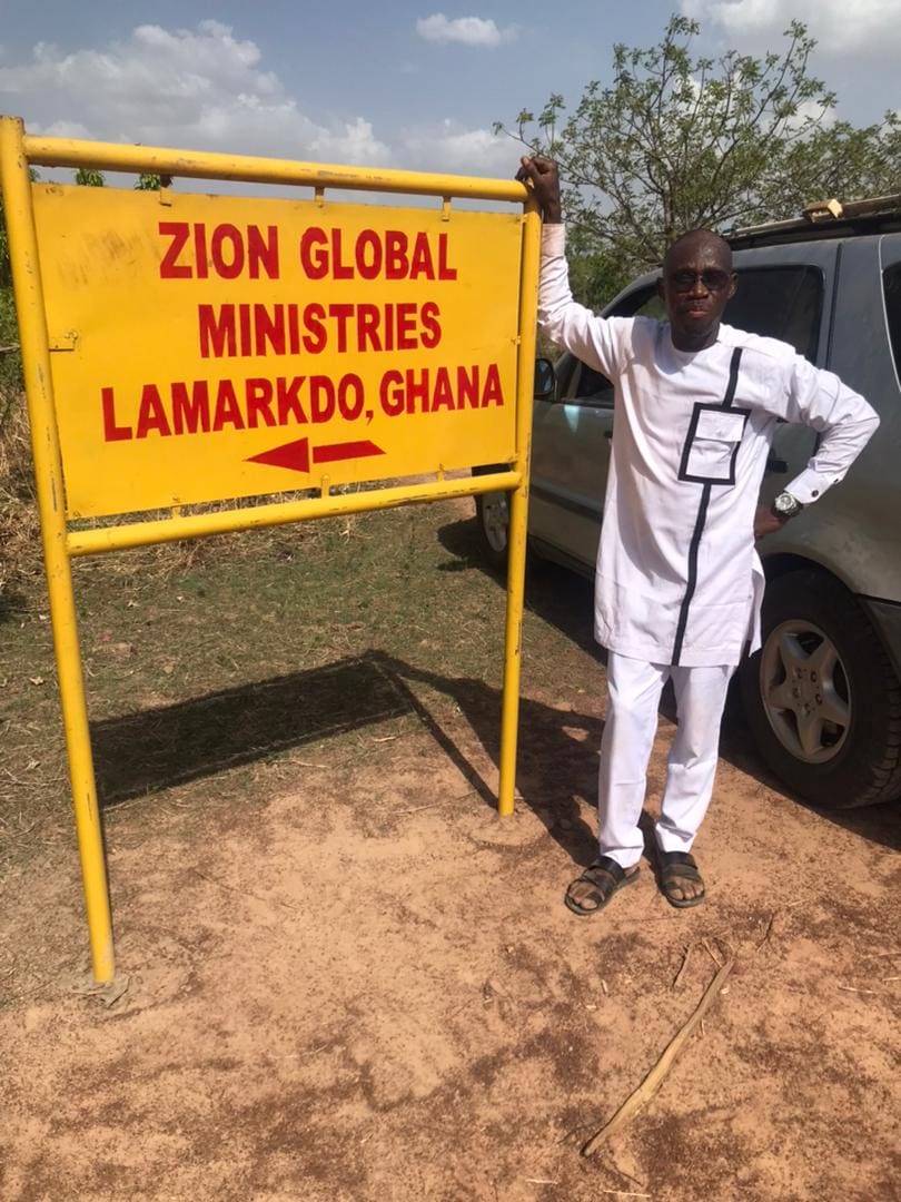 Person by Zion Global Ministries sign, Lamarkdo Ghana